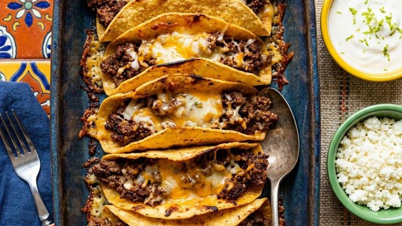 Row of golden oven-baked cheesy tacos in a baking dish topped with melted cheese and fresh toppings